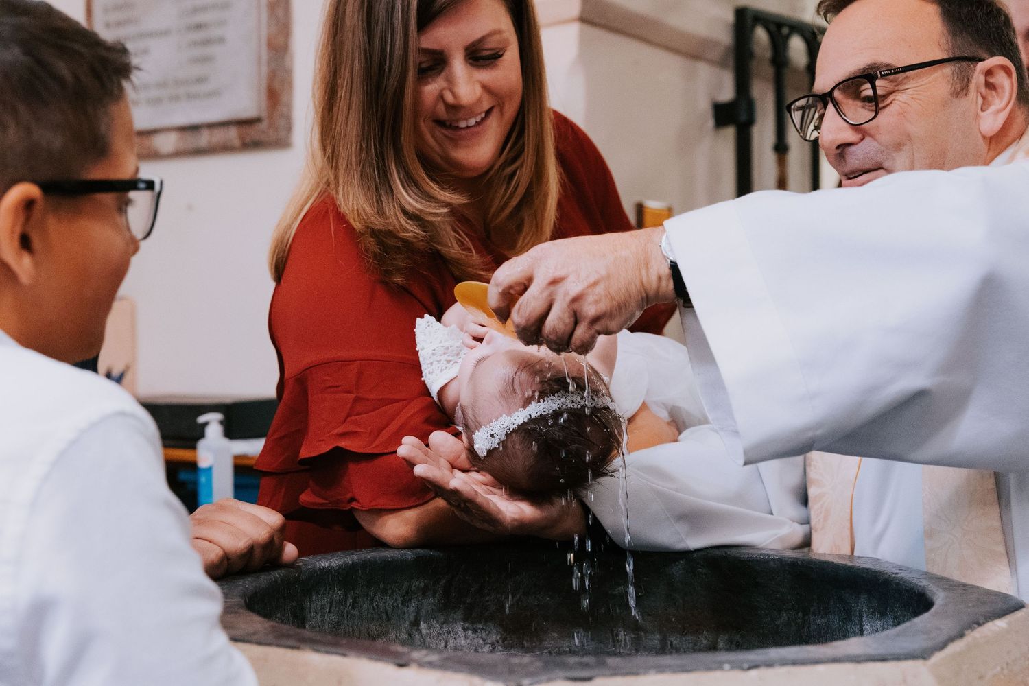 A group participates in a baptismal ceremony around a stone font in a church setting.