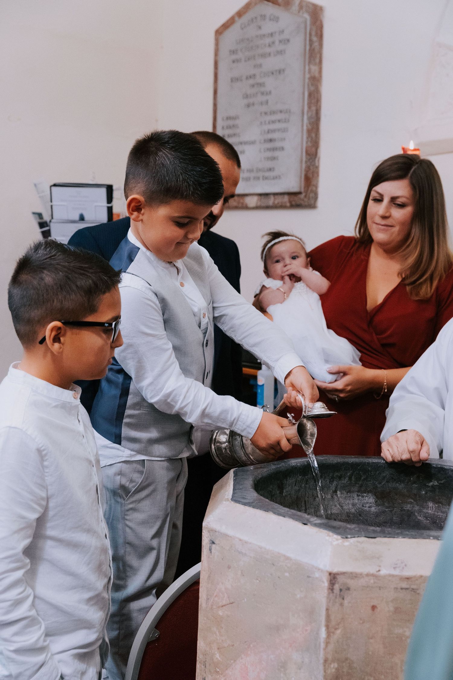 A young boy in white clothing participates in a baptismal ritual at a church font.