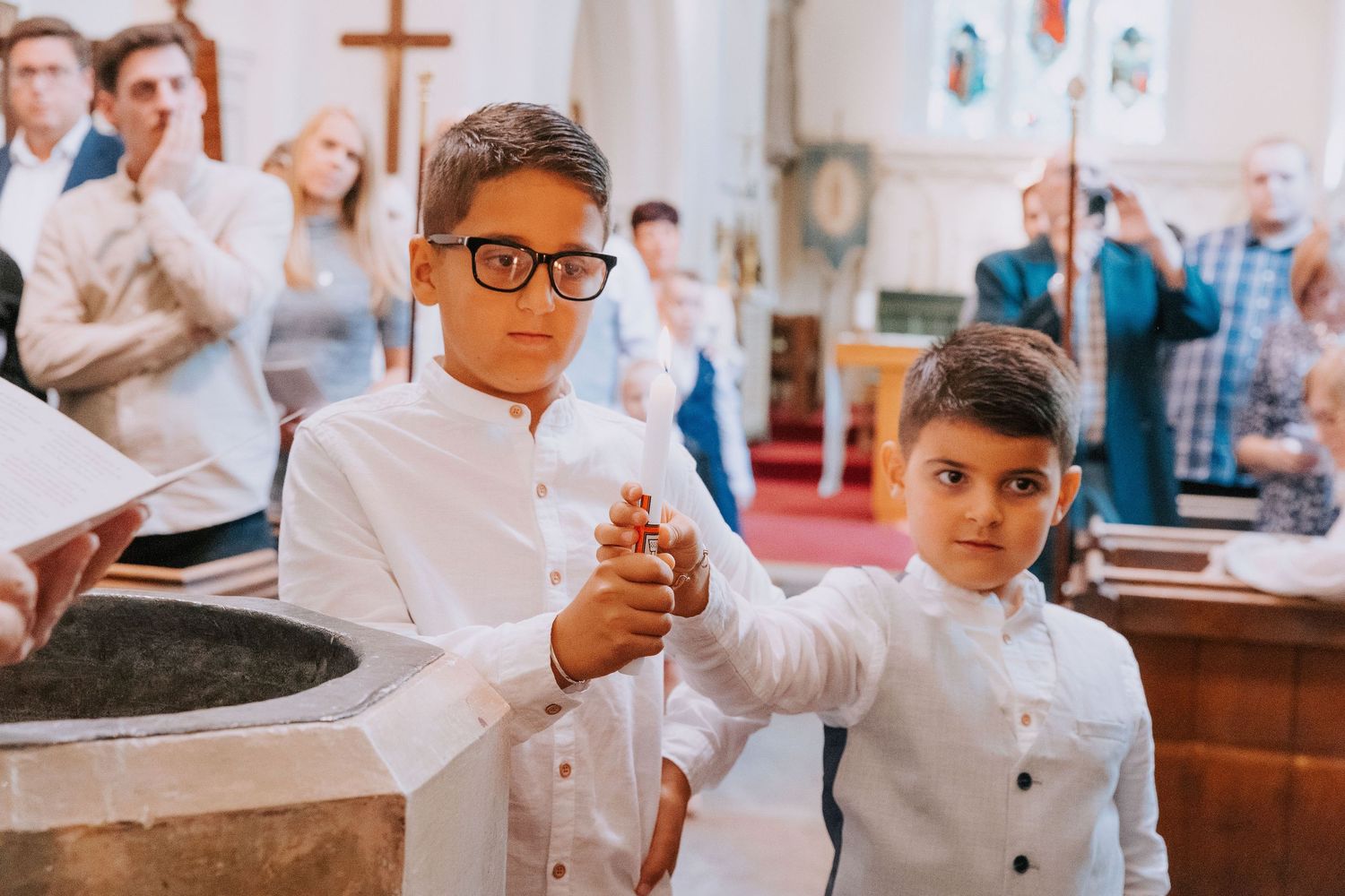 People in white clothing gather around a baptismal font during a church ceremony.