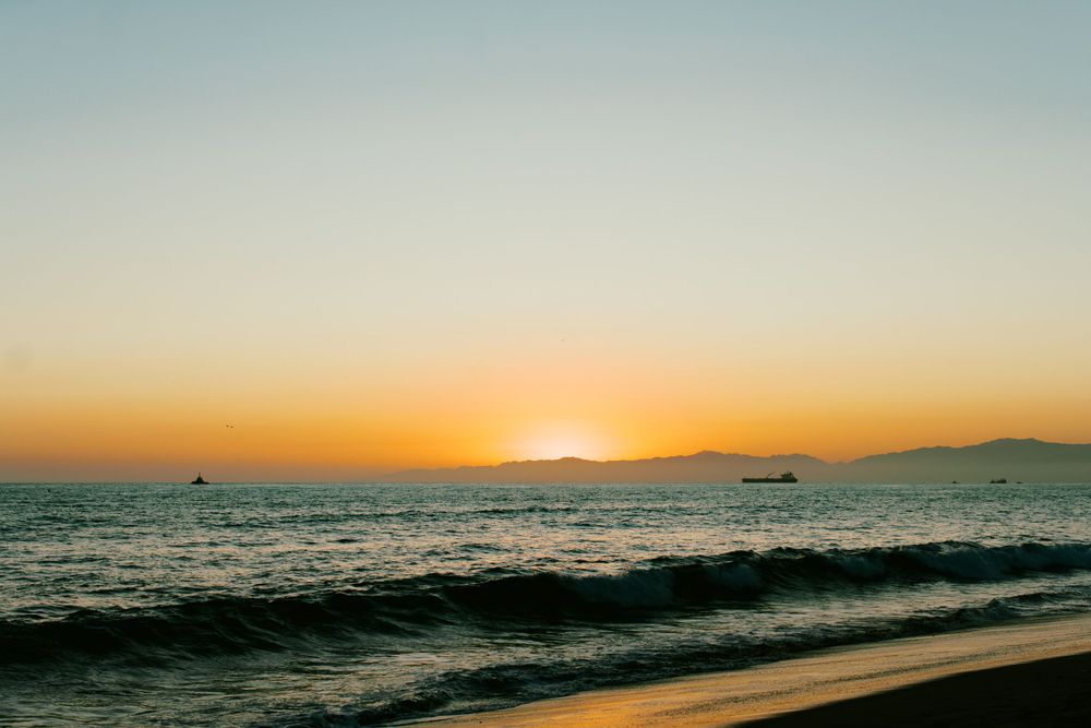 A vibrant orange sunset over the ocean with boats on the horizon.