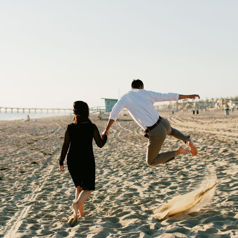 A playful moment captured as two people run and jump along the beach at sunset.