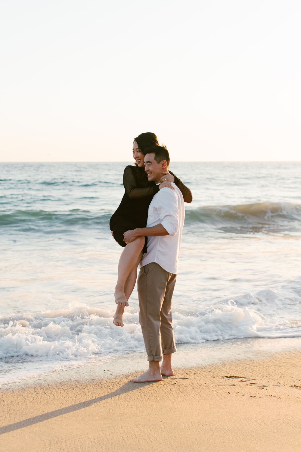 A romantic beach scene with one person carrying another as waves crash on the shore.