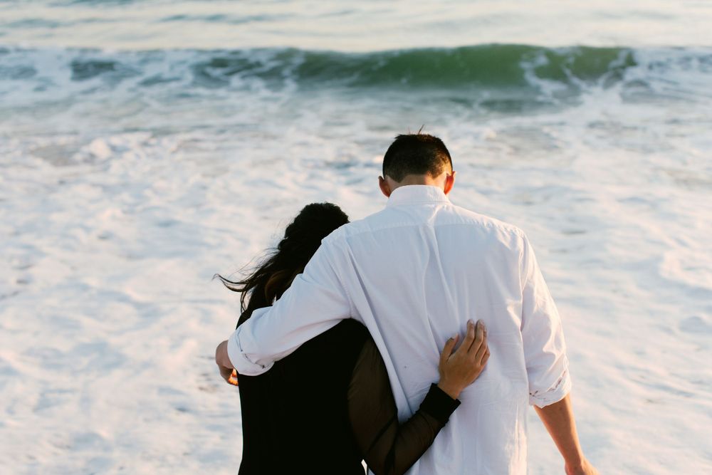 A couple embraces while watching ocean waves crash on the shore.