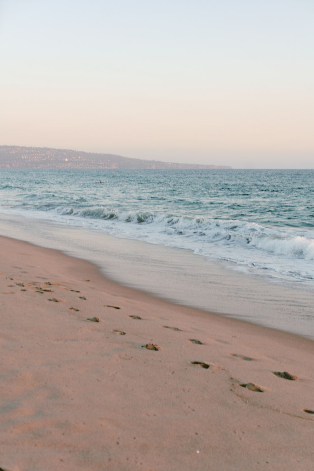 Serene beach landscape with rolling waves and footprints in the sand at sunset.
