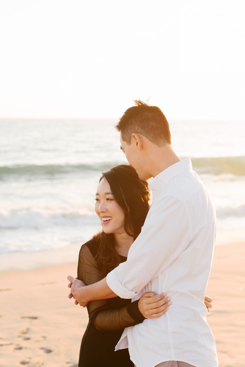 A loving moment shared between a couple on a sunny beach with waves in the background.