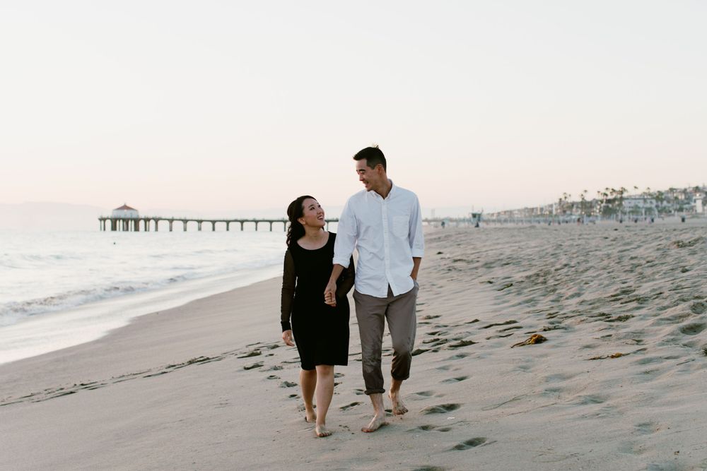 A couple takes a romantic beach walk together at dusk with a pier in the background.