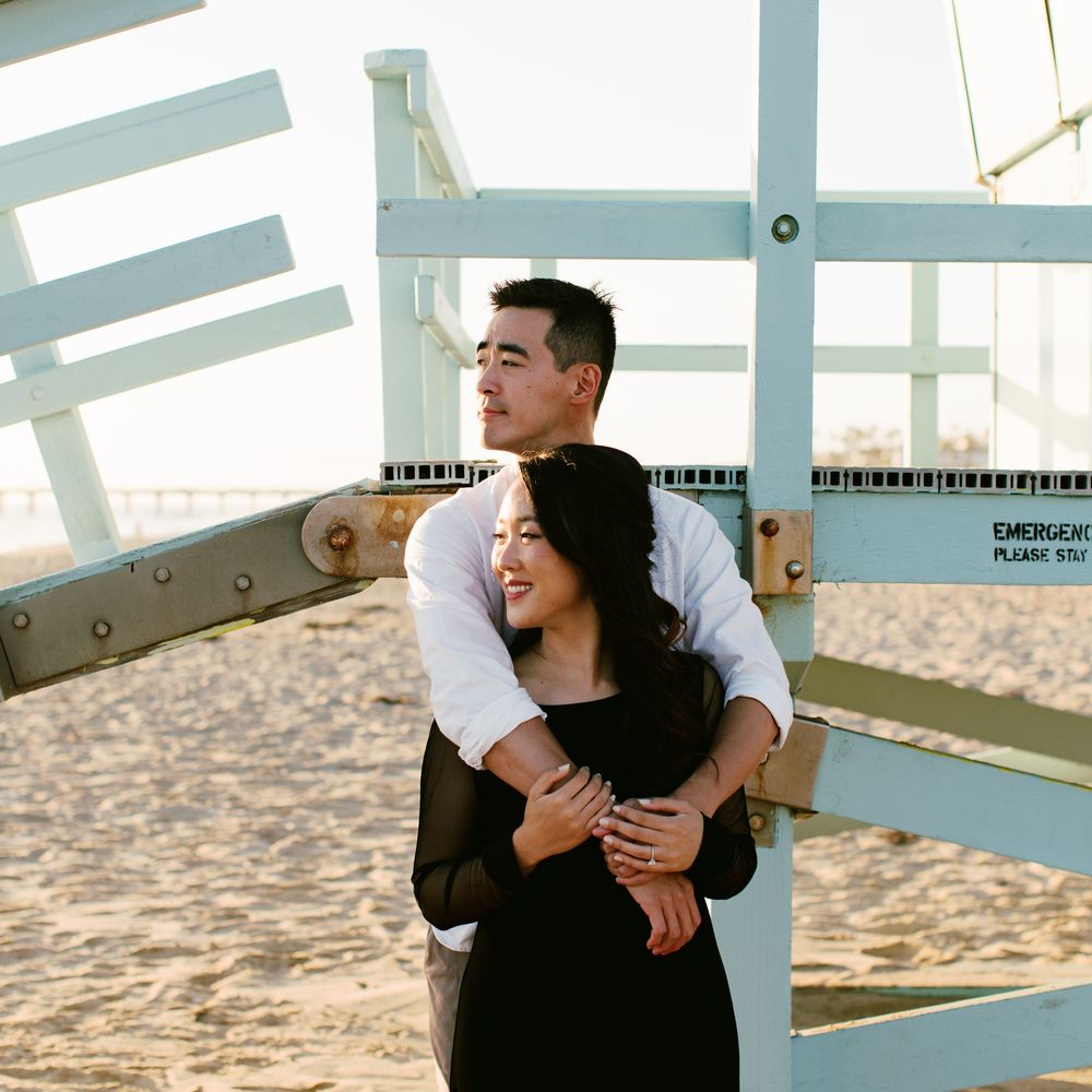 A romantic embrace in front of a lifeguard tower on the beach during golden hour.