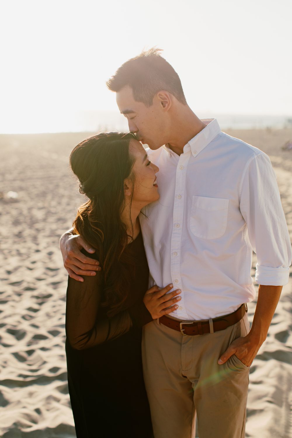 Intimate couple embracing on a sandy beach during golden hour.