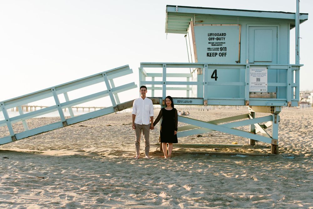 Couple posing by blue lifeguard tower number 4 on sandy beach at golden hour.
