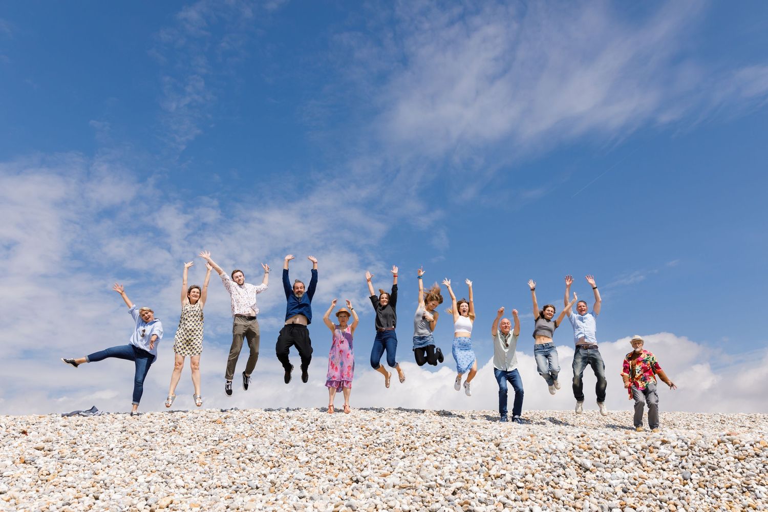 Group of people jumping in unison against a bright blue sky on a sunny beach during a family beach photoshoot