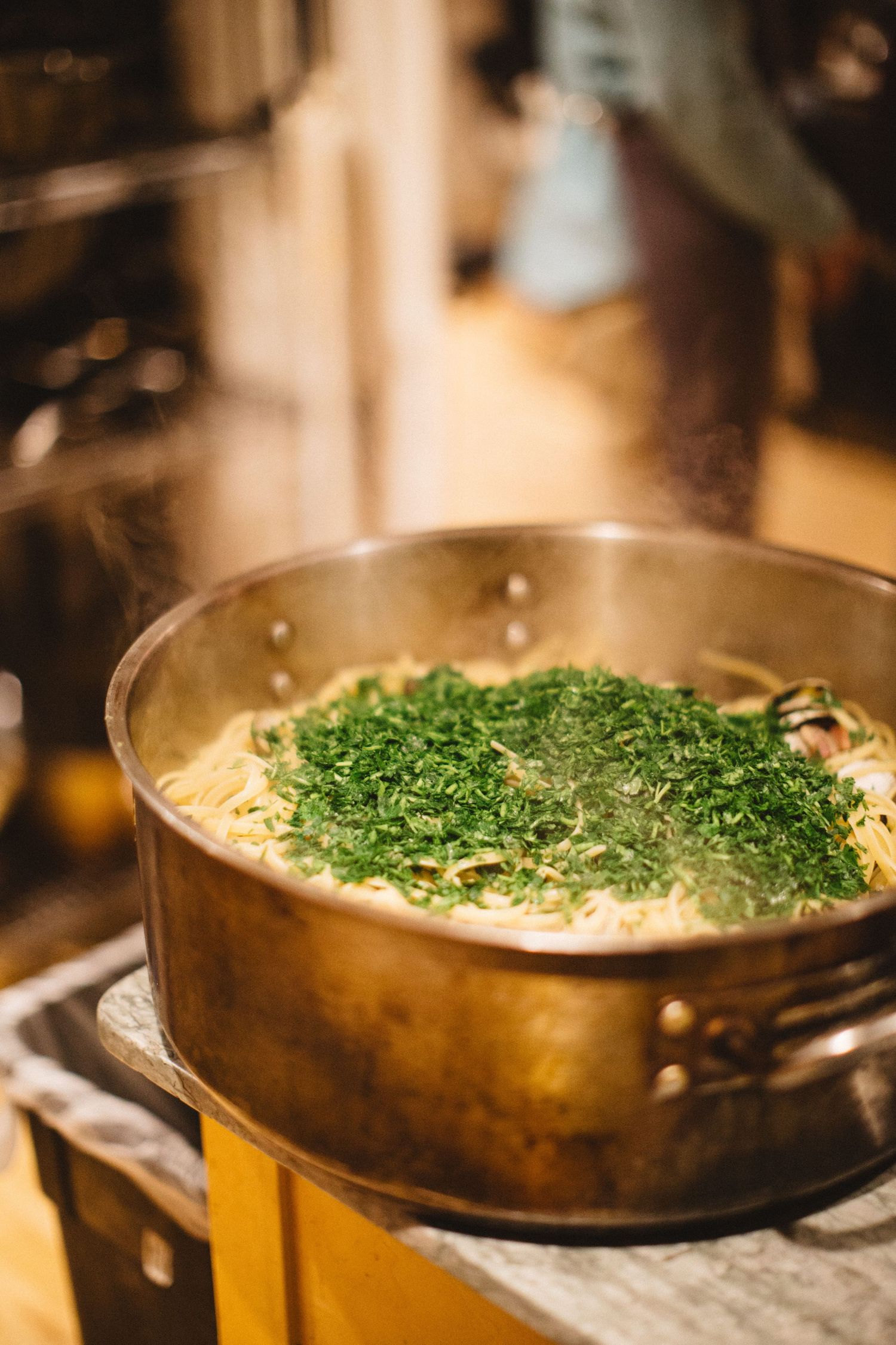Fresh herbs garnish a large pot of cooking pasta on a stovetop.