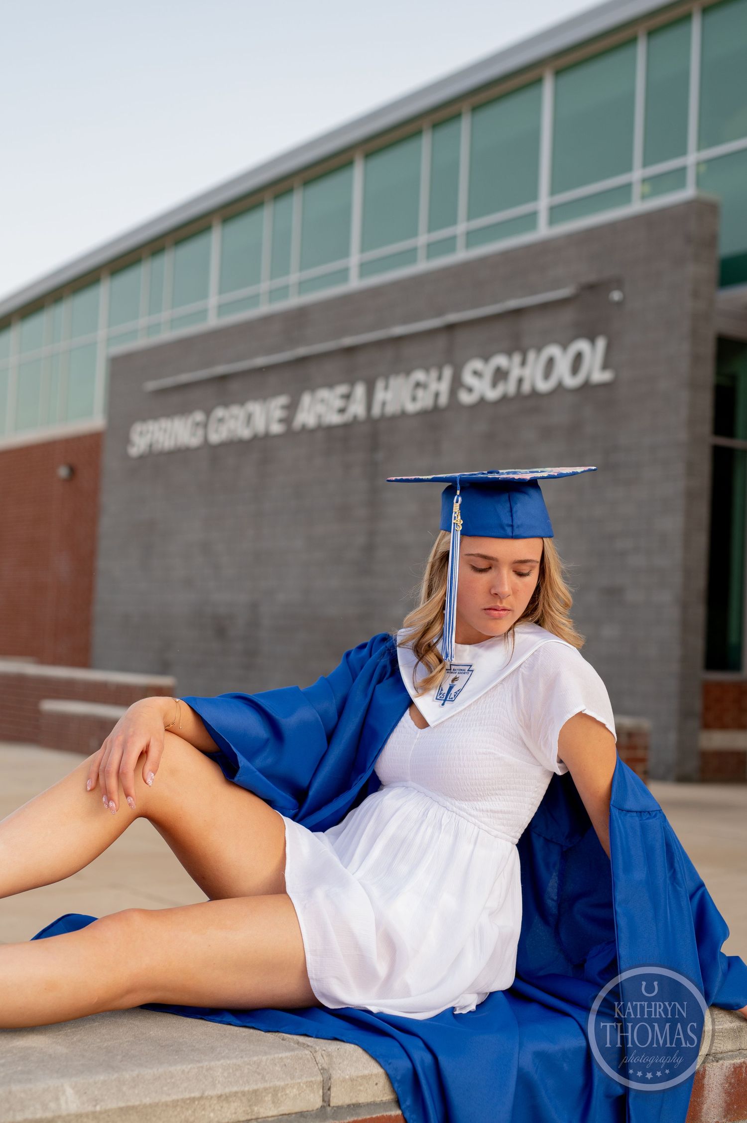 Graduate in blue cap and white dress reclines on steps during graduation photoshoot.