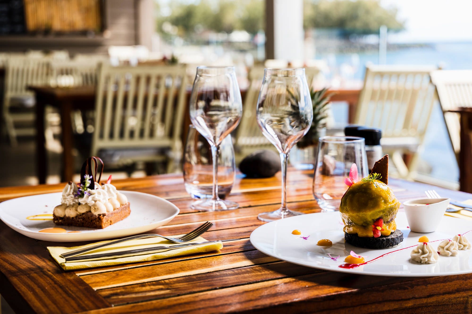Elegant restaurant dining tables set with wine glasses and place settings by waterfront windows.