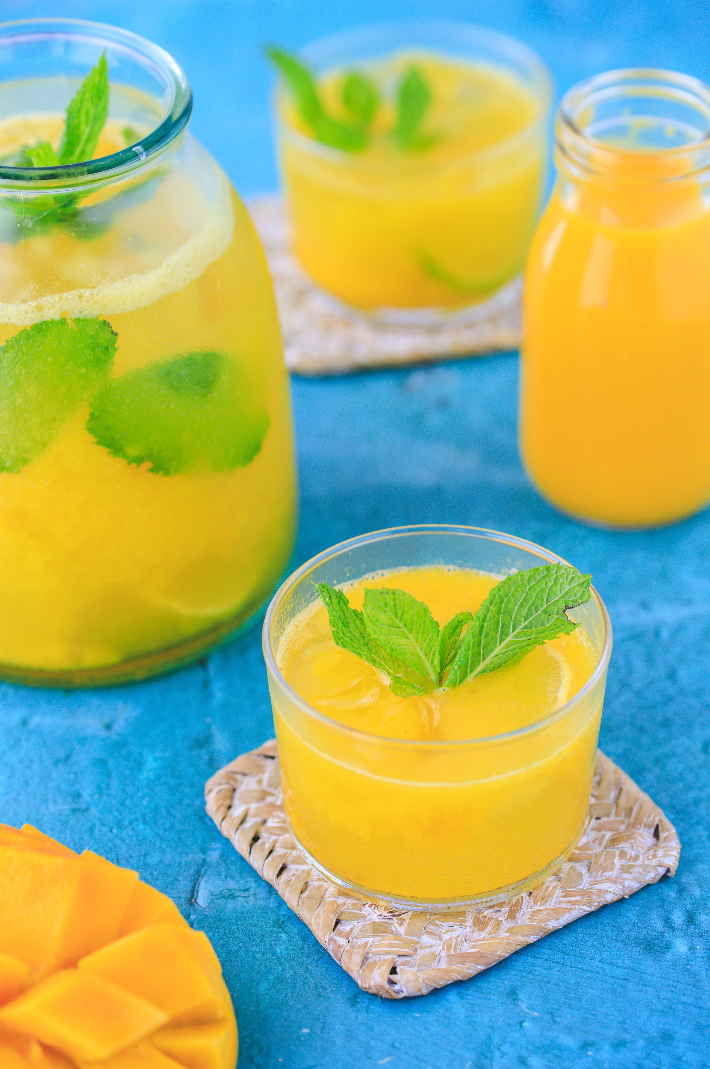 Bright yellow mango smoothies garnished with mint leaves on blue background.