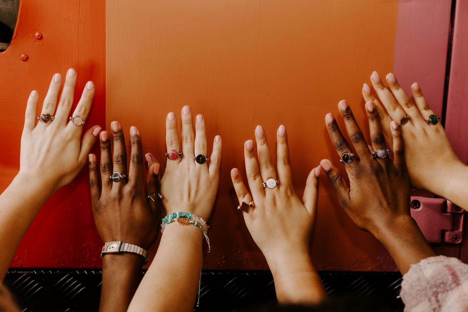 Multiple hands raised showing rings against bright orange background.