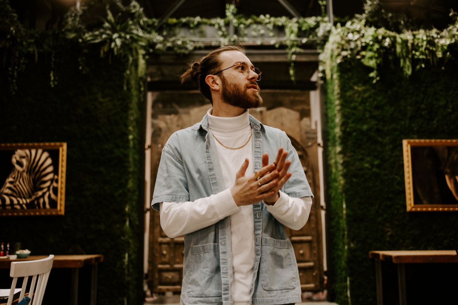 Casual portrait in garden setting with vine-covered pergola and wooden chairs.