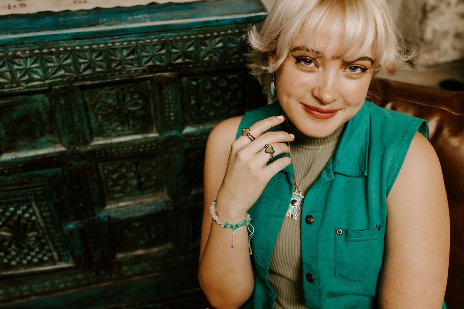 Woman in green sleeveless top showing off jewelry against vintage backdrop.