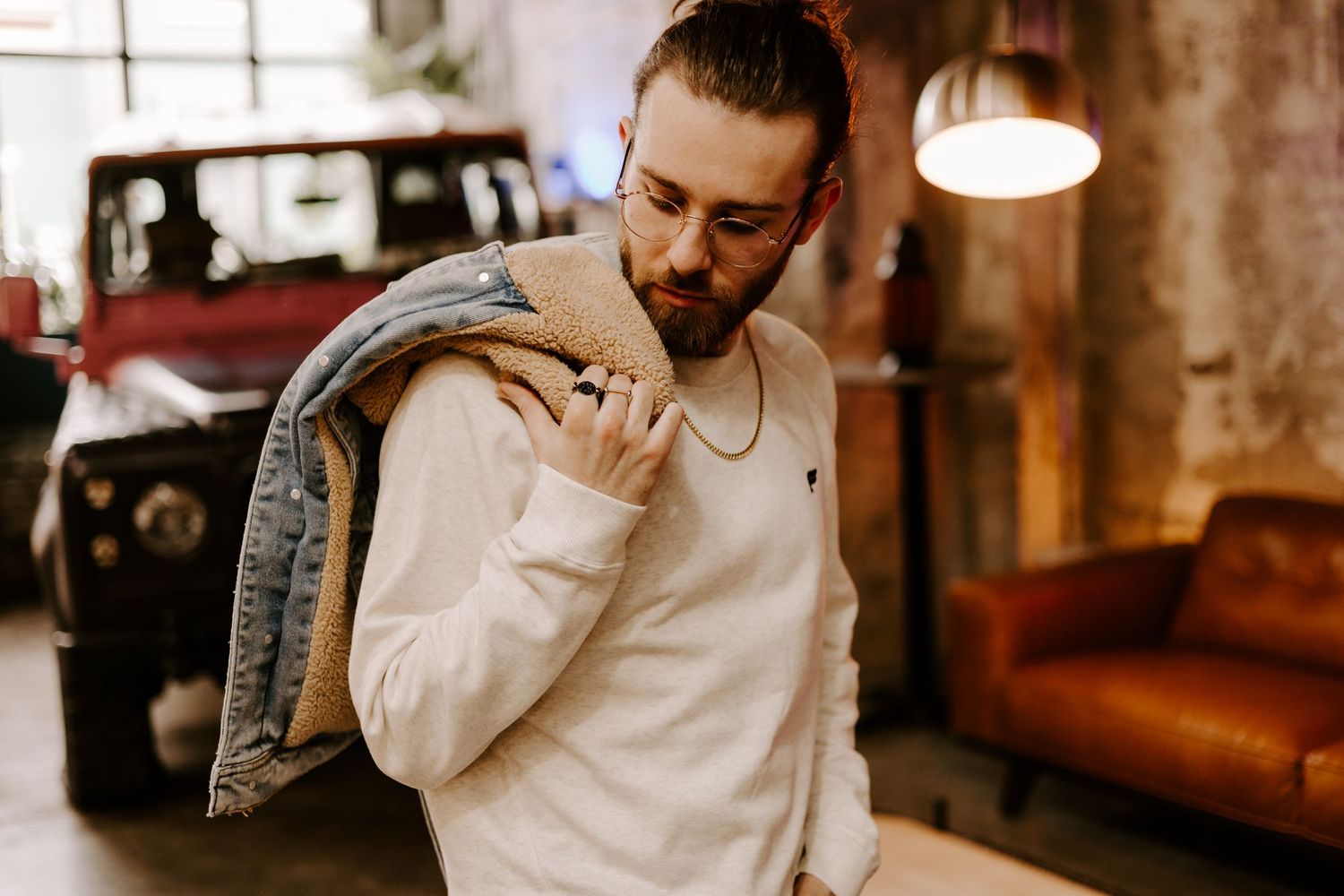Man in white tank top carrying denim jacket on shoulder in industrial setting.