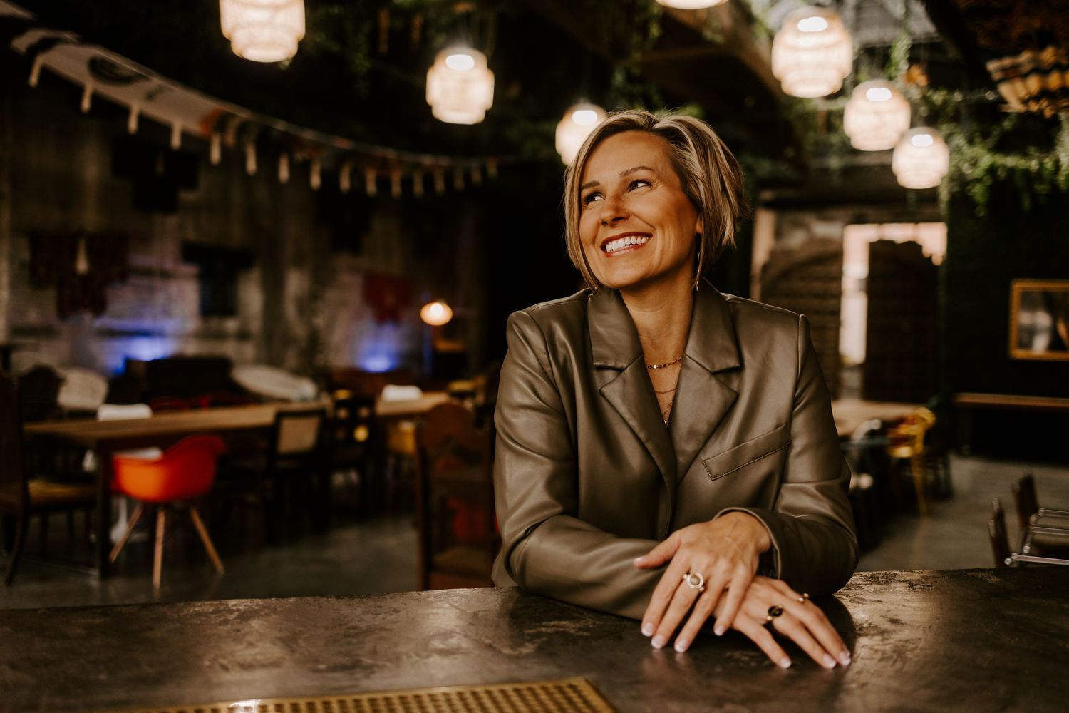 Professional portrait in warm-lit restaurant setting with hanging lanterns and ambient lighting.
