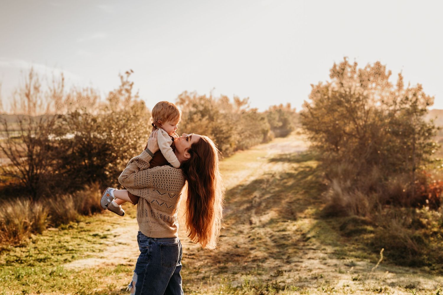 Mother holding son up in grassy field.