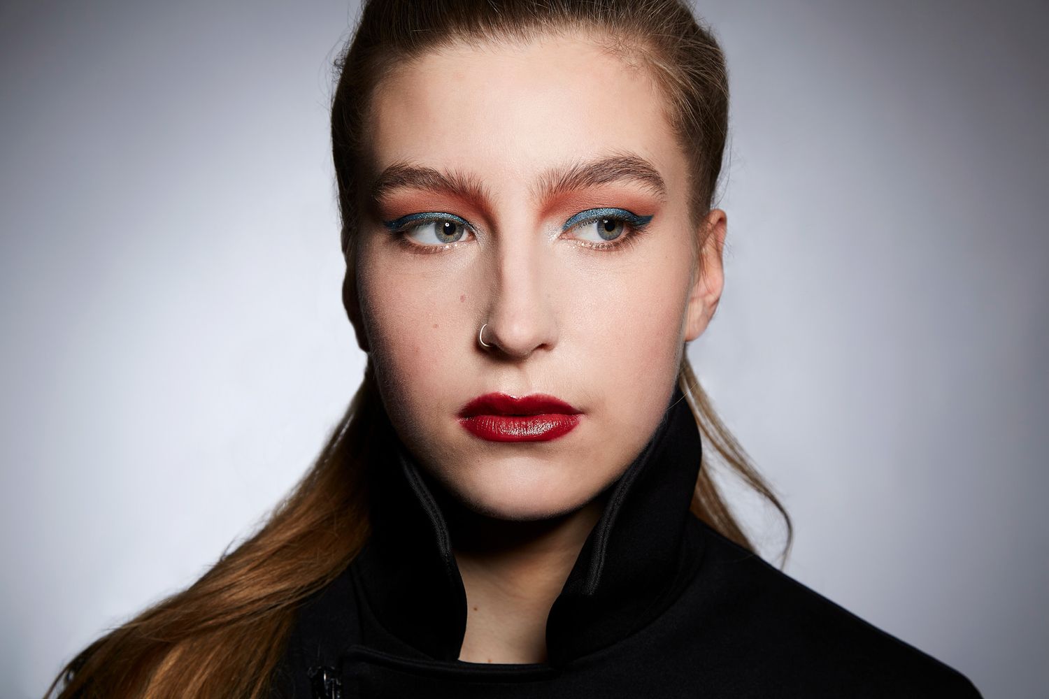 Beauty portrait showing dramatic makeup with bold red lips against grey studio background.
