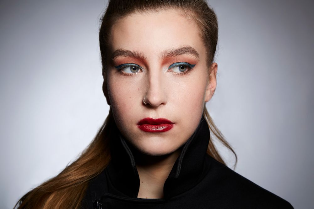 Beauty portrait showing dramatic makeup with bold red lips against grey studio background.