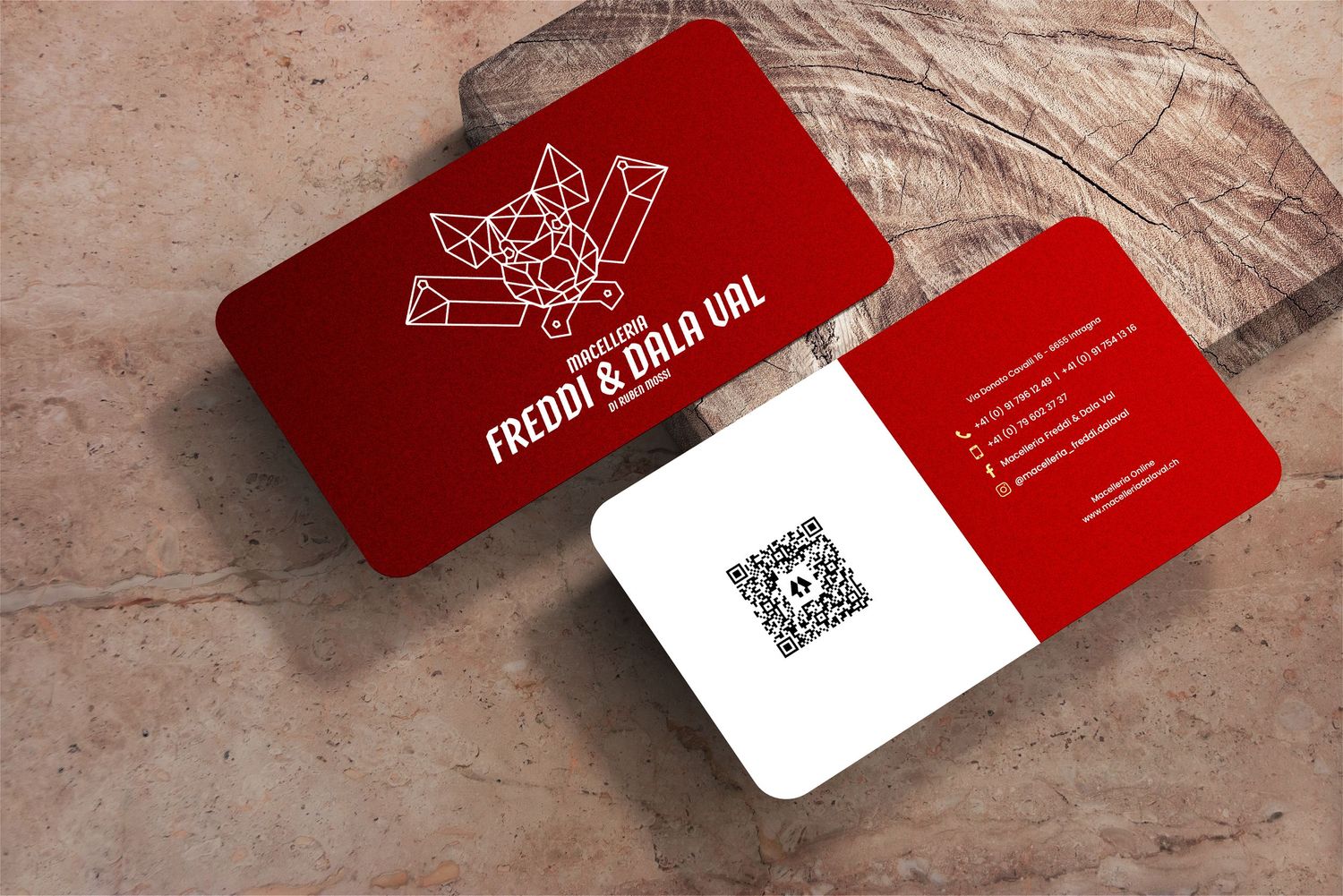 Red and white business cards with geometric fox design and QR code displayed on wooden surface.