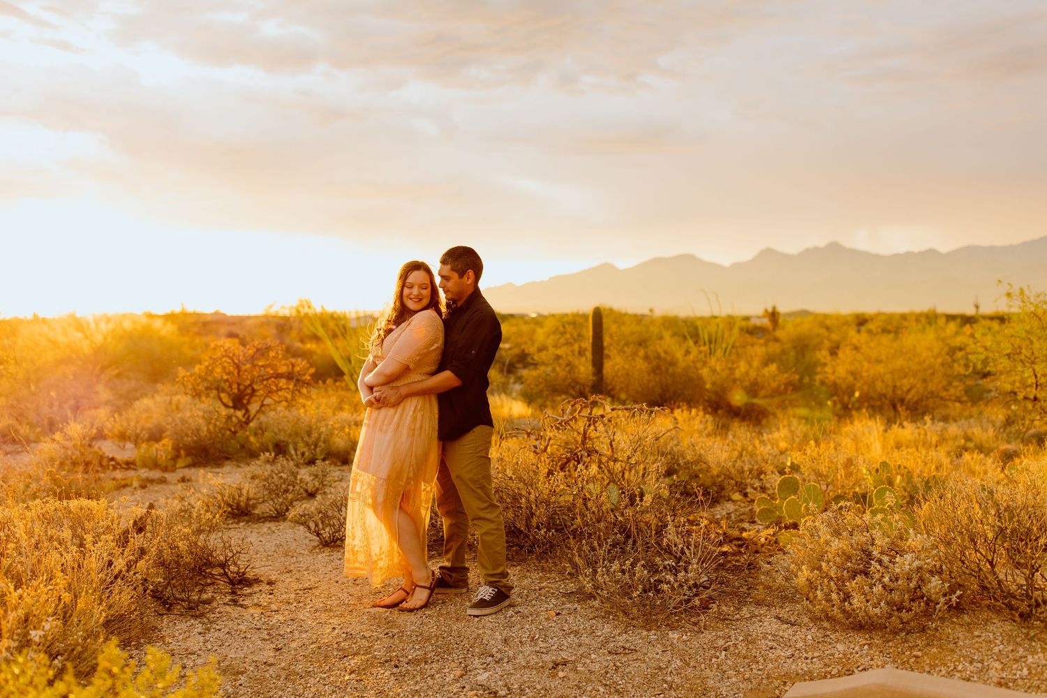 A couple embraces in a desert landscape during golden hour sunset.
