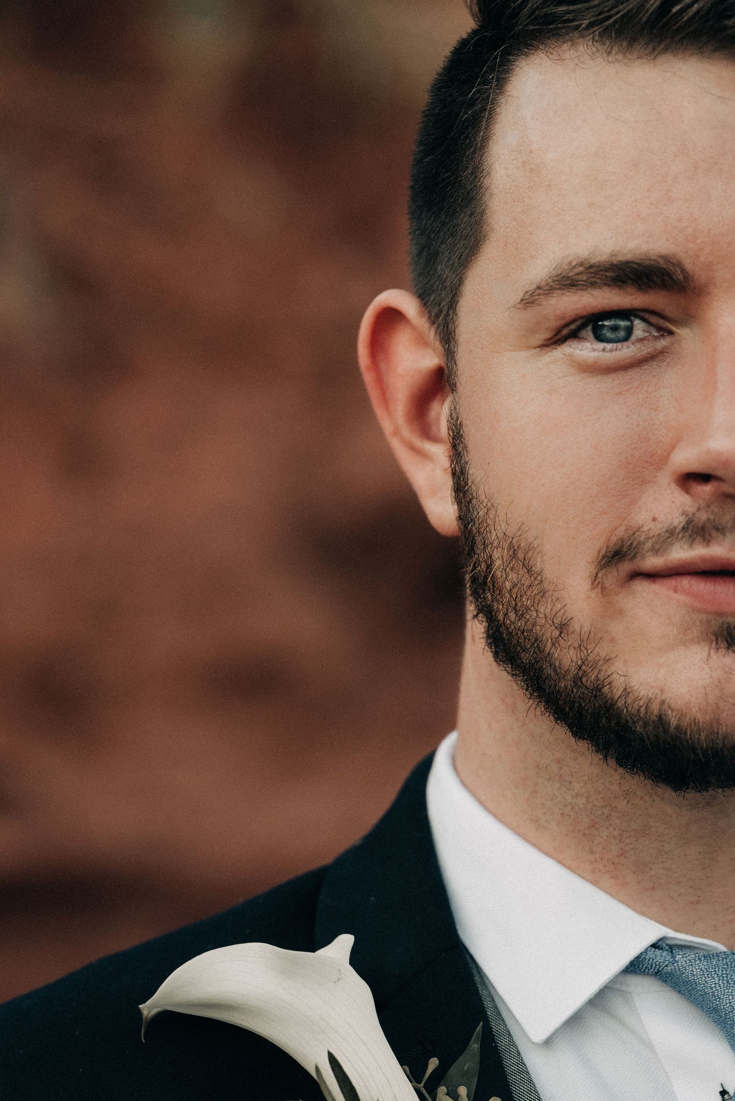 Close-up portrait showing blue eyes and formal attire with a white boutonniere.