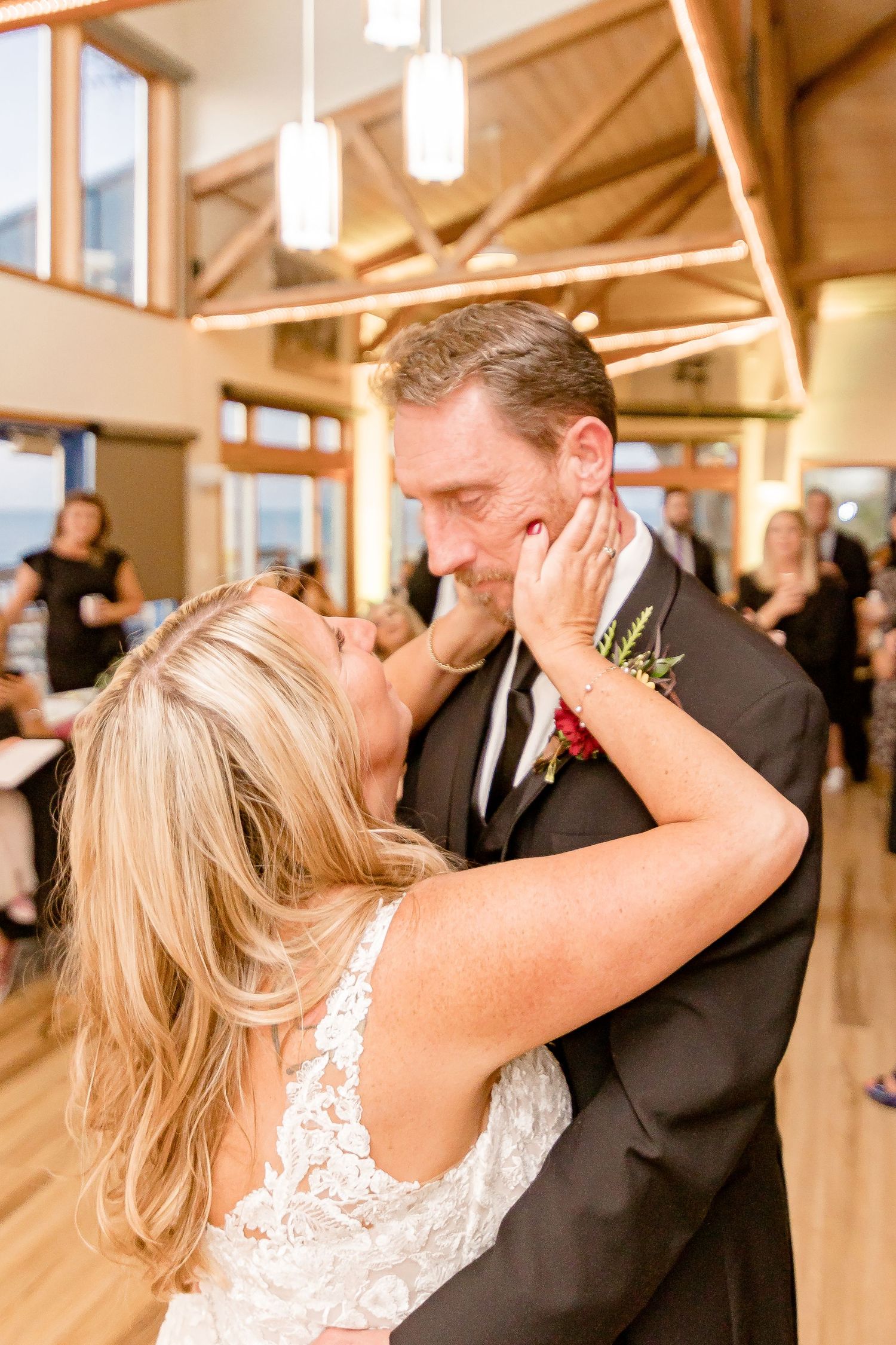 Bride and groom share an intimate dance moment in a warmly lit reception venue with exposed wooden beams.