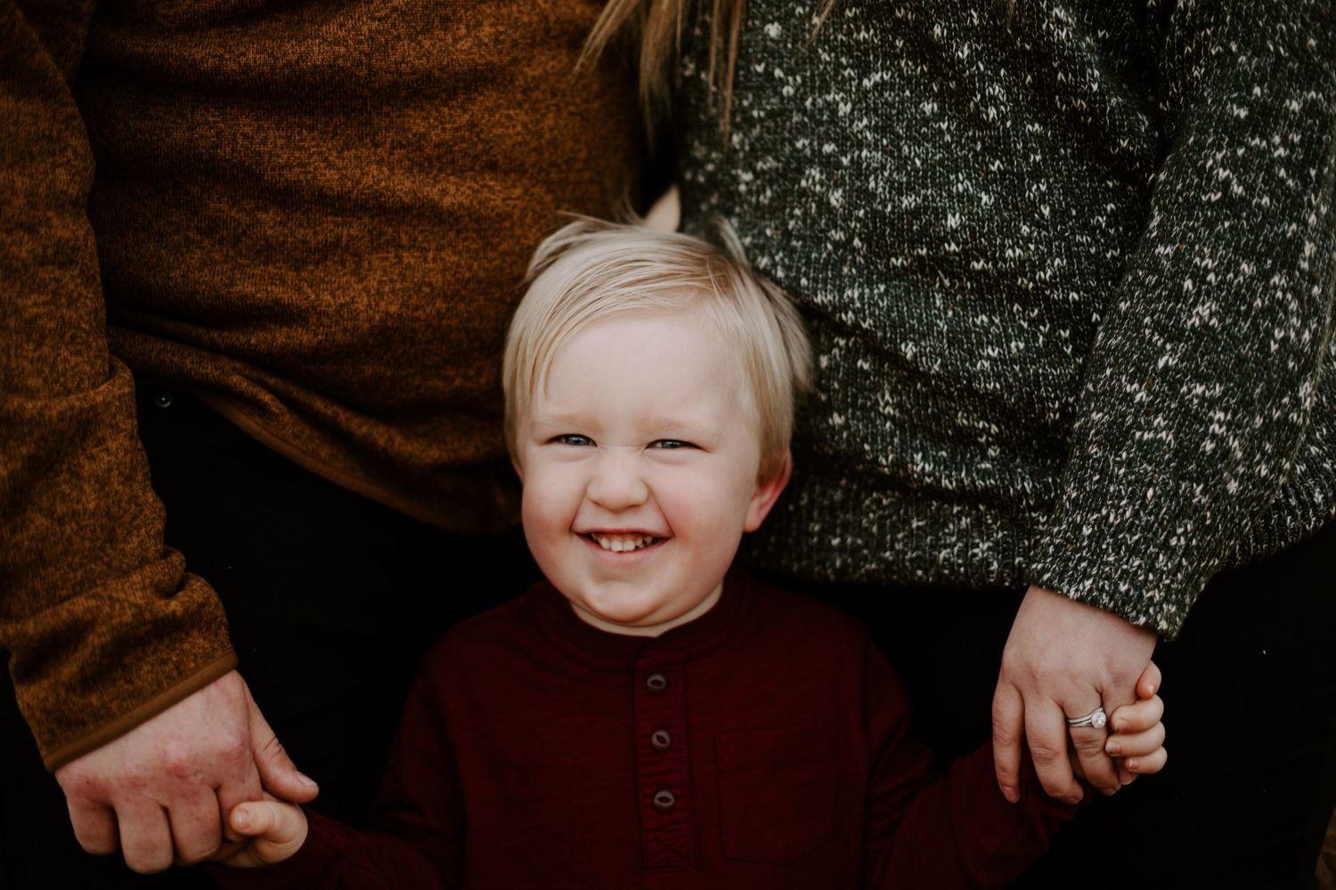 A boy smiling holding hands with his parents