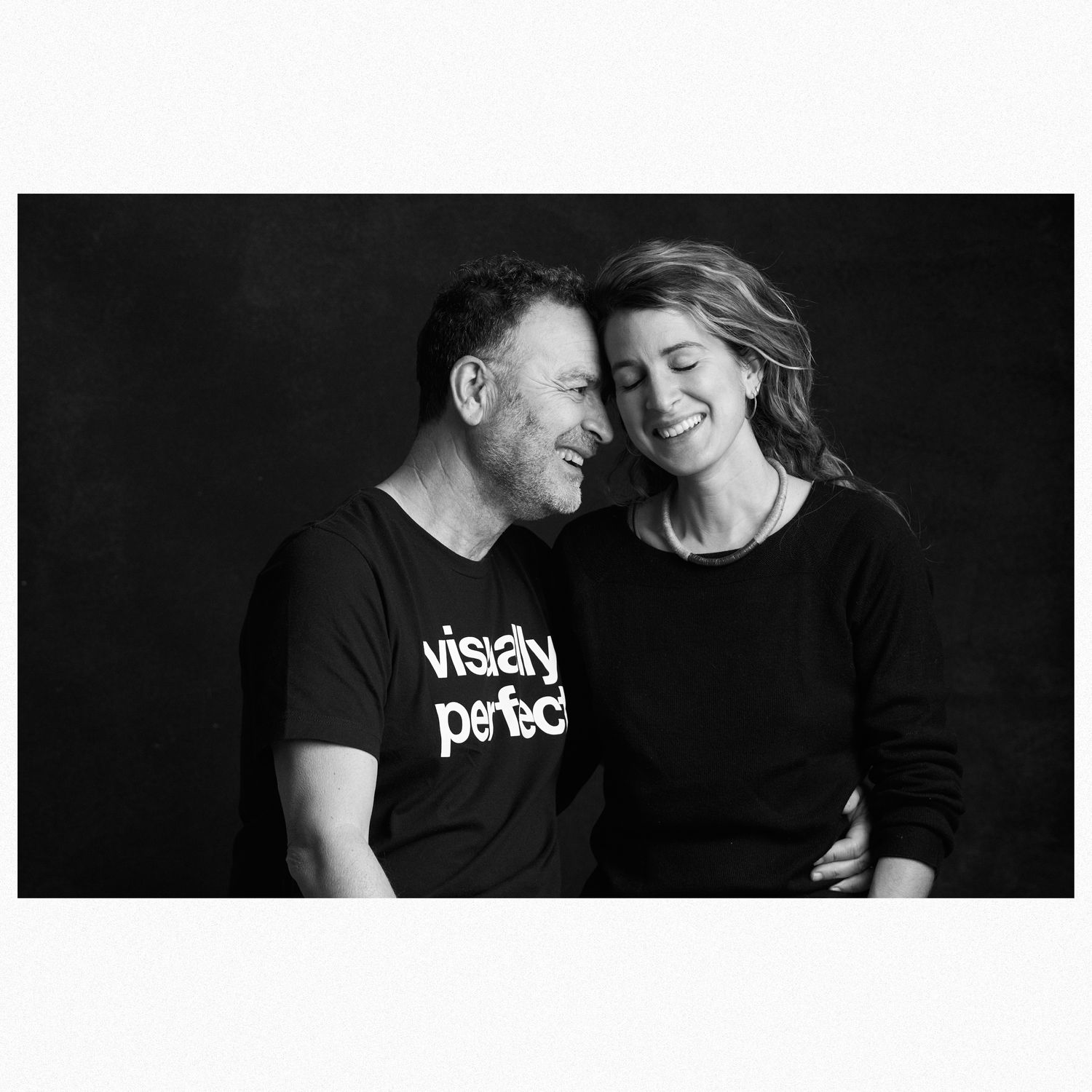 Black and white portrait of a couple in dark clothing sharing an intimate moment.