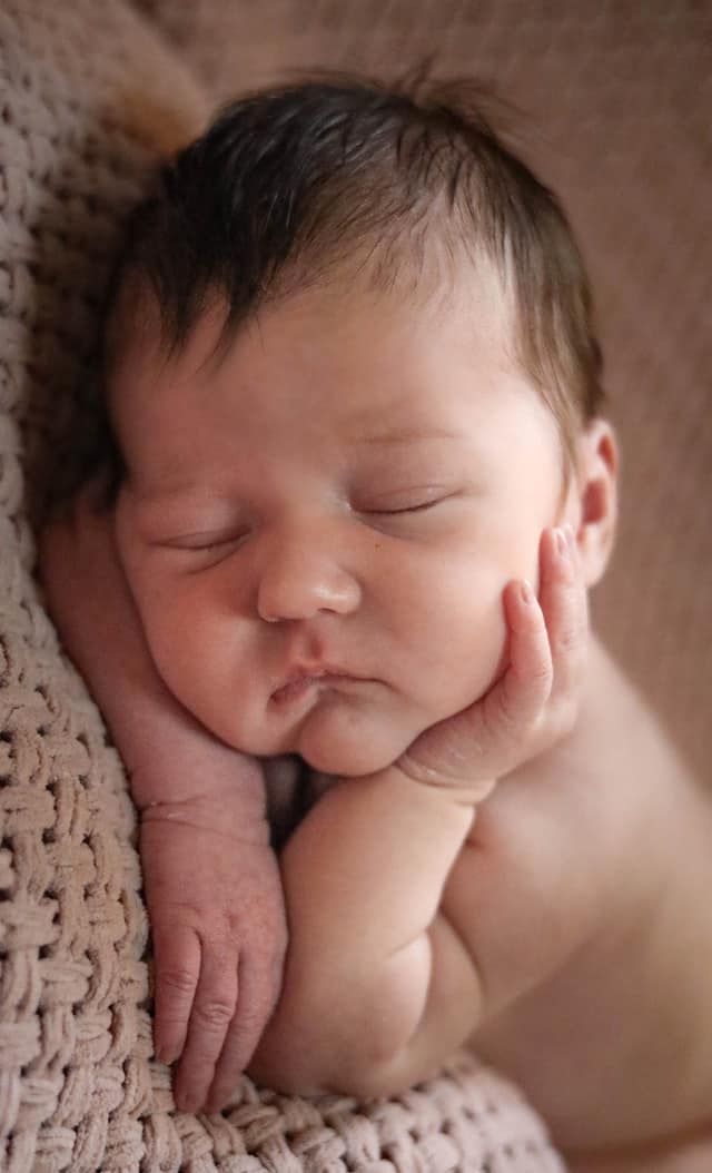 Sleeping newborn baby on soft knit blanket in warm neutral tones.
