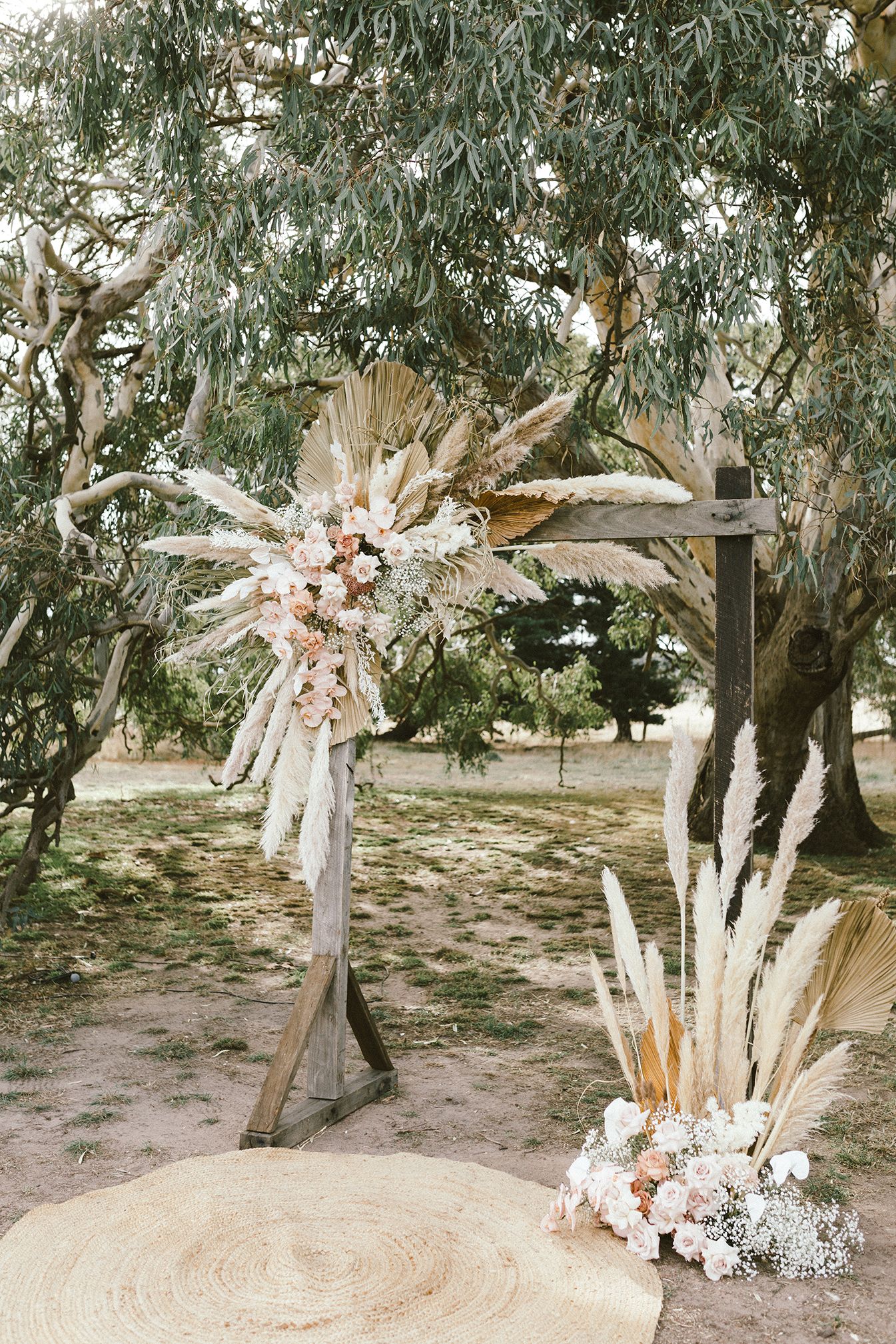 Bohemian wedding arch decorated with dried flowers and pampas grass under eucalyptus trees.