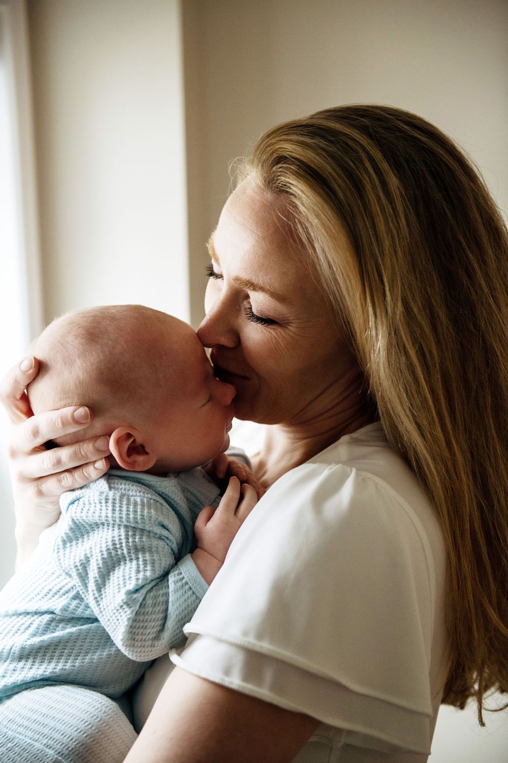 A tender moment between parent and infant as they share a gentle kiss in natural window light.
