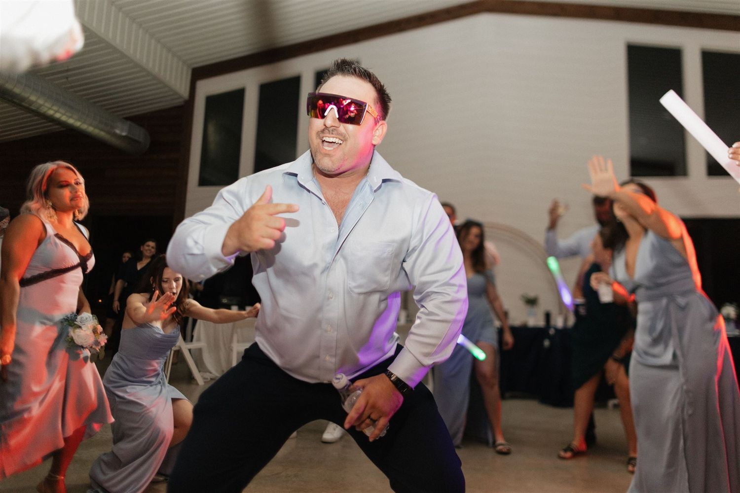Guest wearing sunglasses strikes a dramatic dance pose at wedding reception.