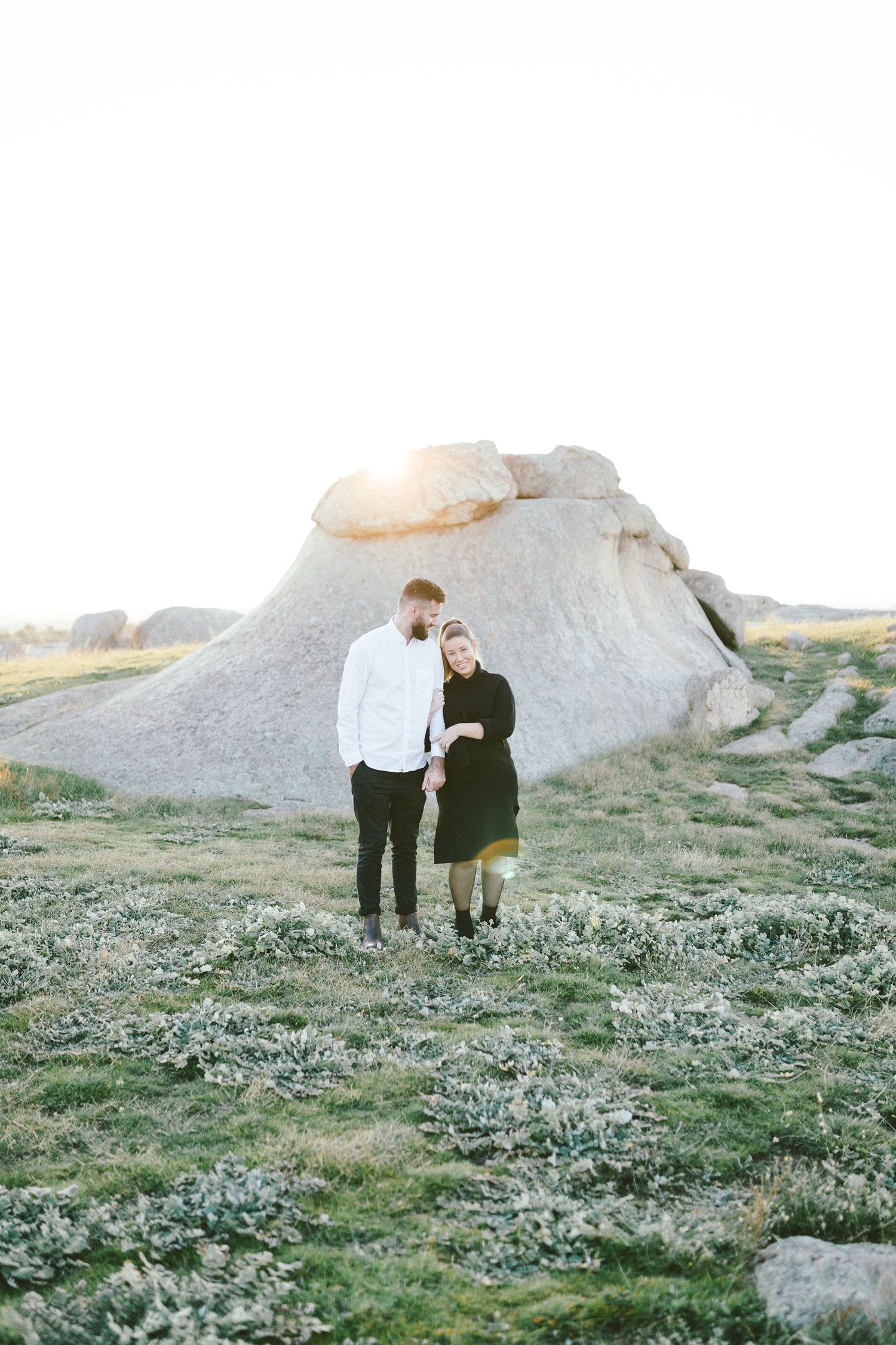 A couple embraces near a large white rock formation surrounded by desert vegetation.