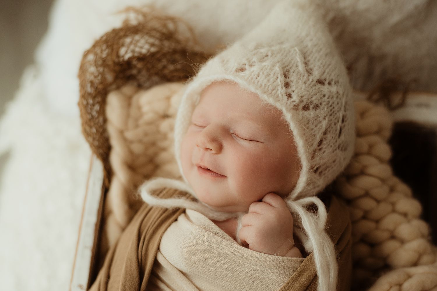 Peaceful sleeping newborn wearing knit bonnet on textured blanket.