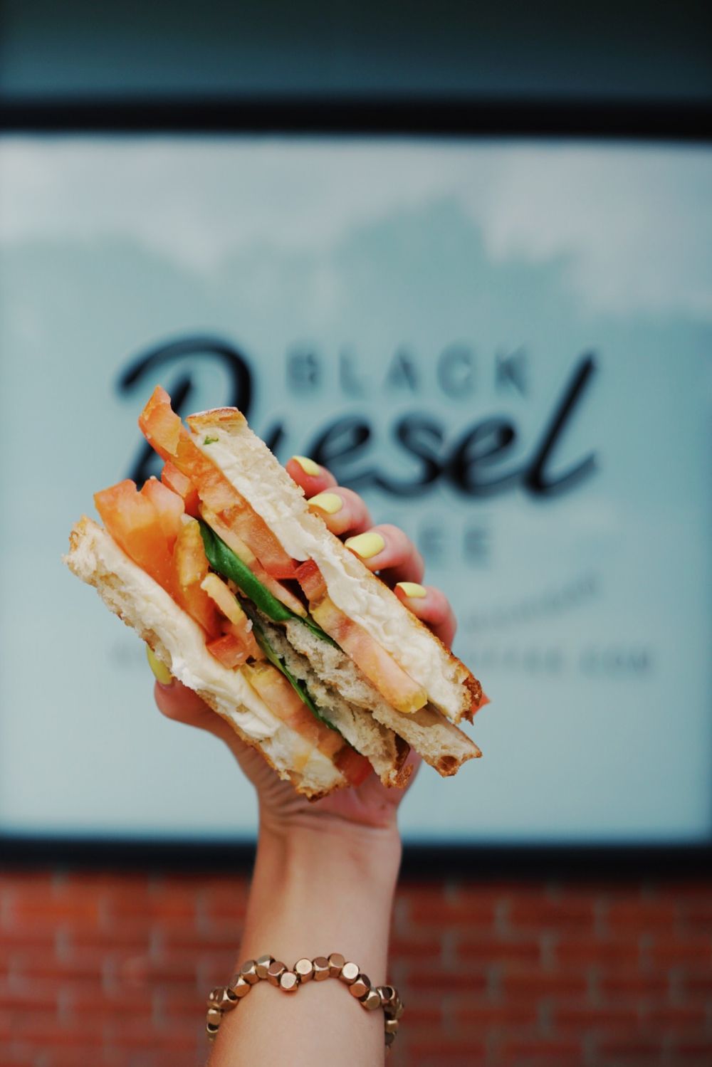 A sandwich held up against a Black Vessel cafe sign shows fresh layers and fillings.