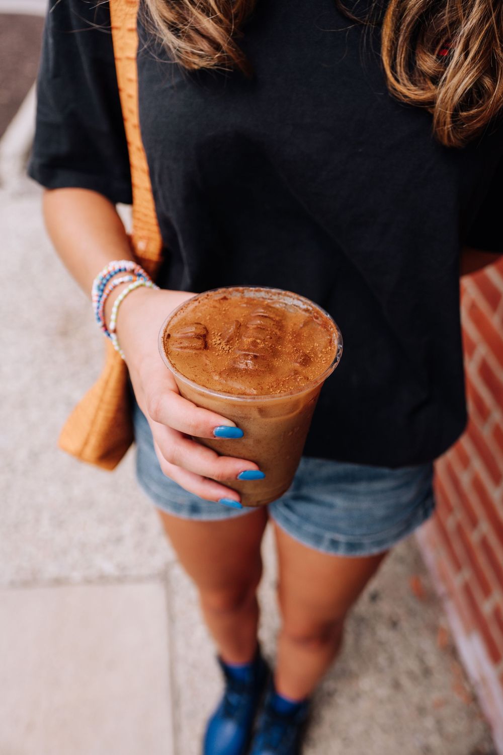Hands holding an iced coffee drink with blue nail polish and casual summer outfit.