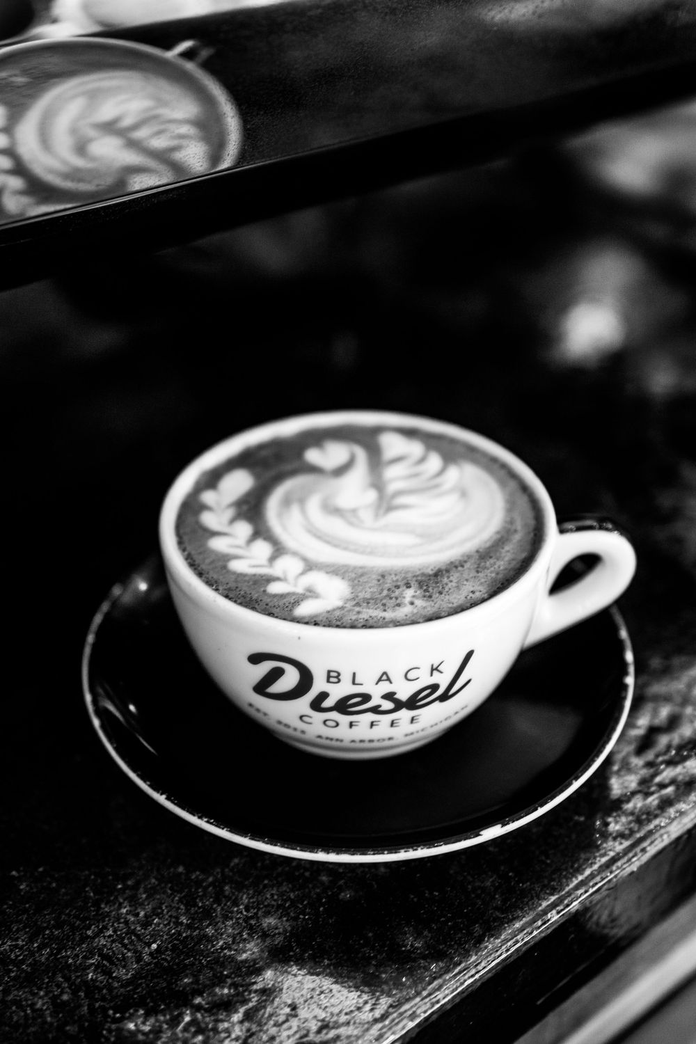 Black and white photo of latte art in a Black Diesel Coffee branded cup.
