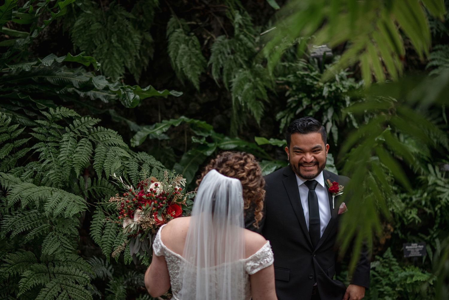 A romantic first look moment in a lush garden setting with ferns.