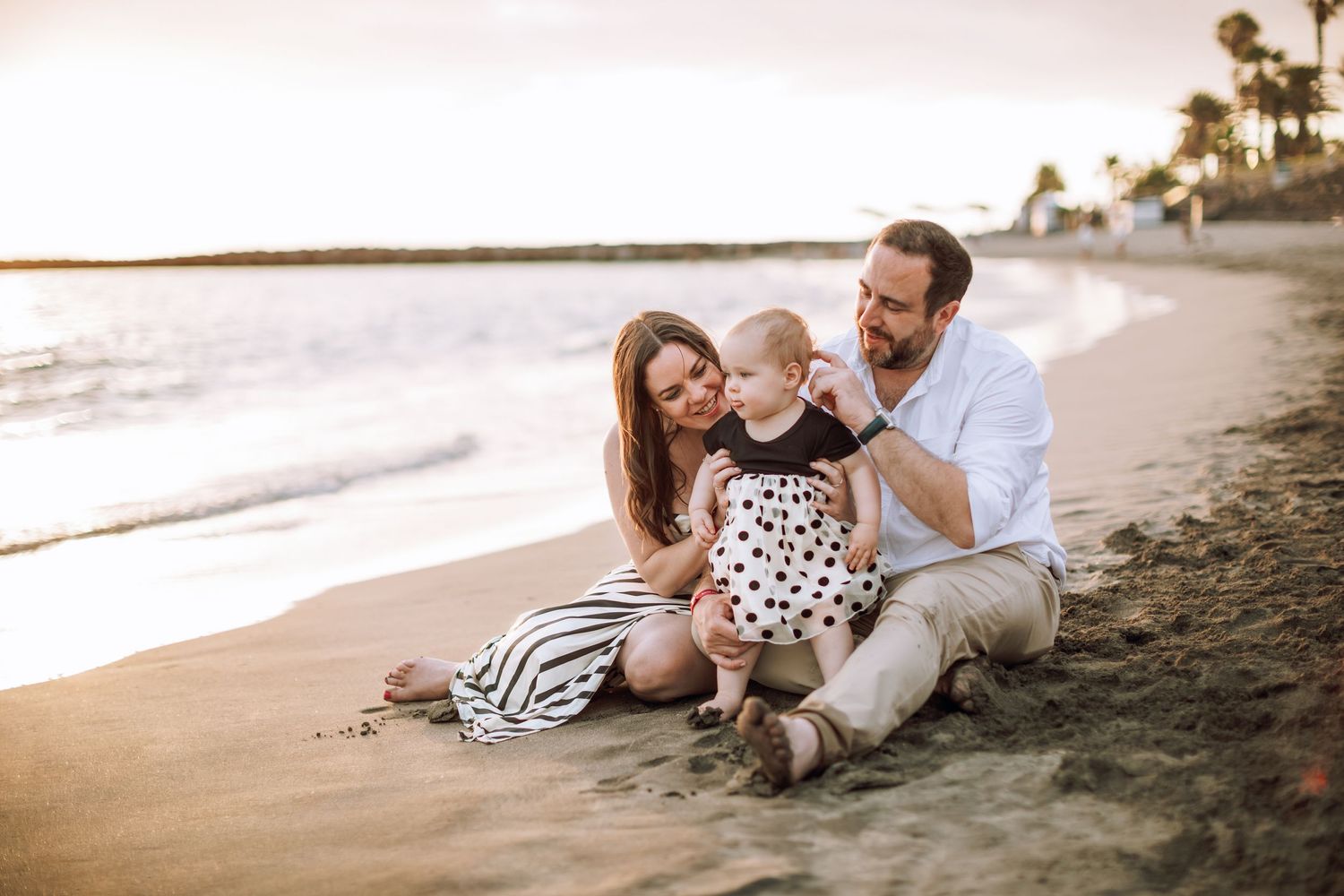 Family of three sitting on the sand and having a sweet moment on a beach at sunset.
