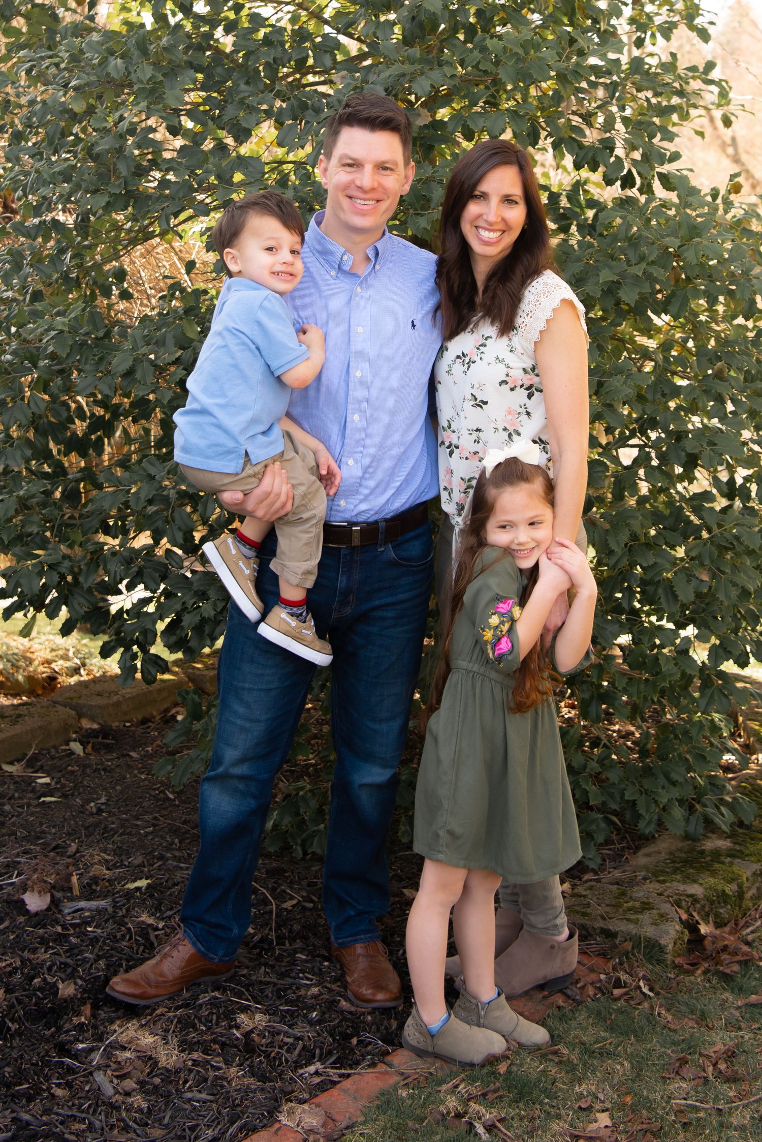 family of four in neutral tones standing in front of a tree