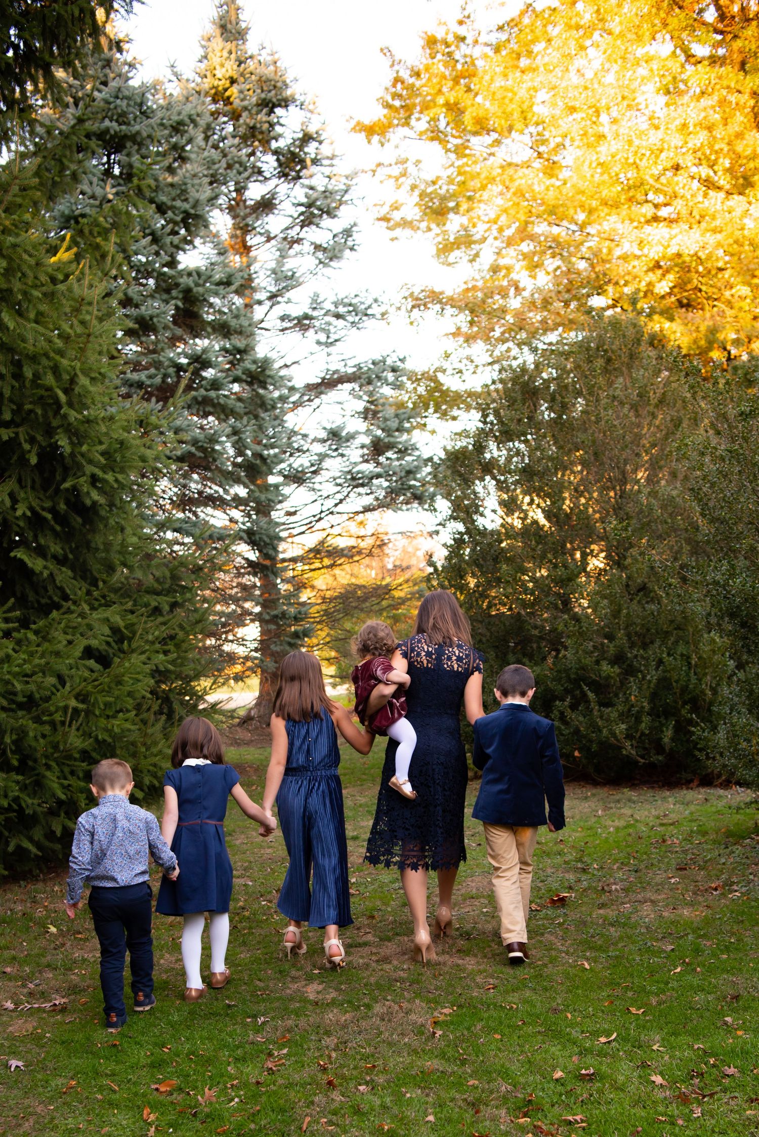 mom and five kids walking towards evergreen trees in hartwood acres park at sunset