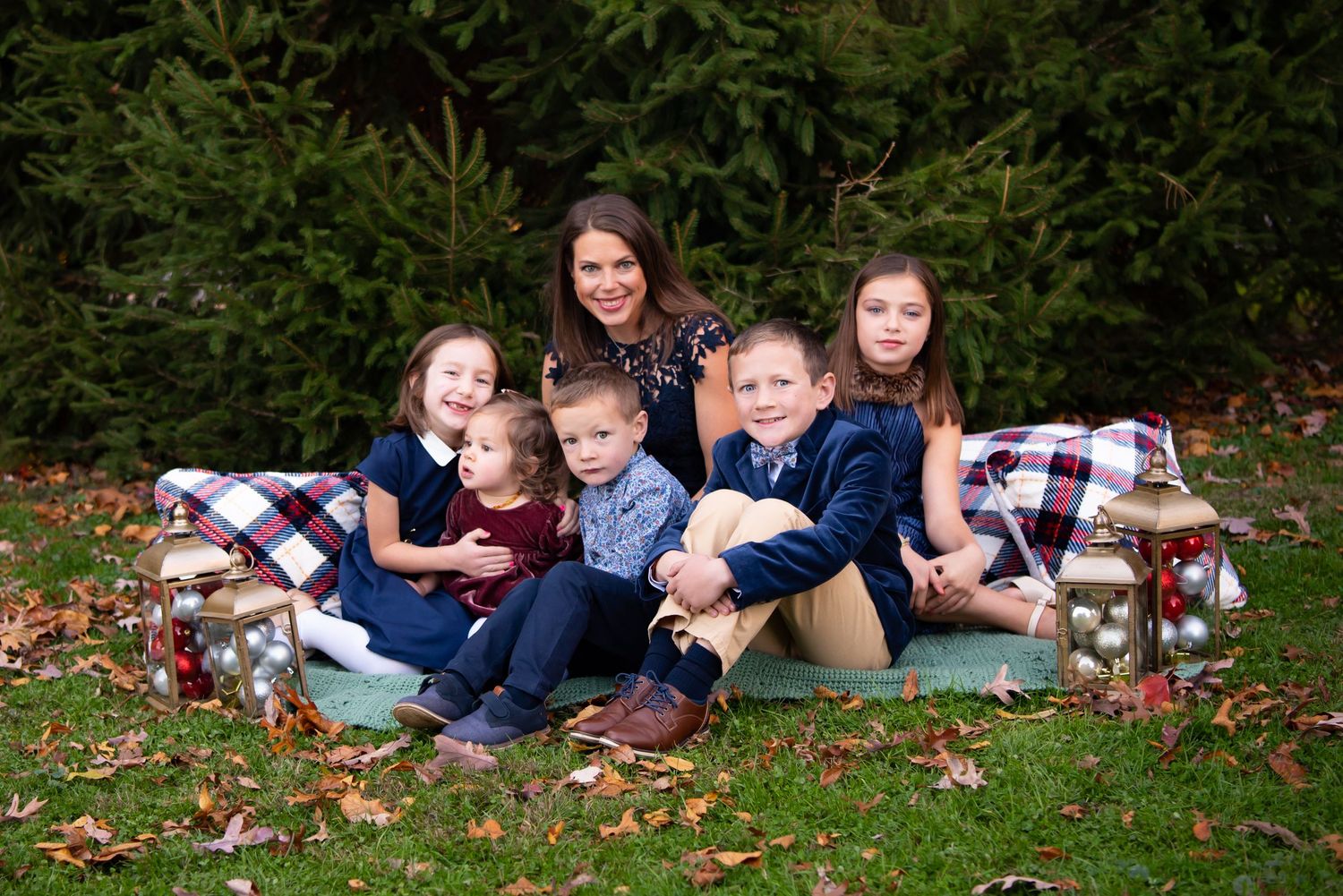 mom and five kids sitting in front of evergreen trees in navy outfits