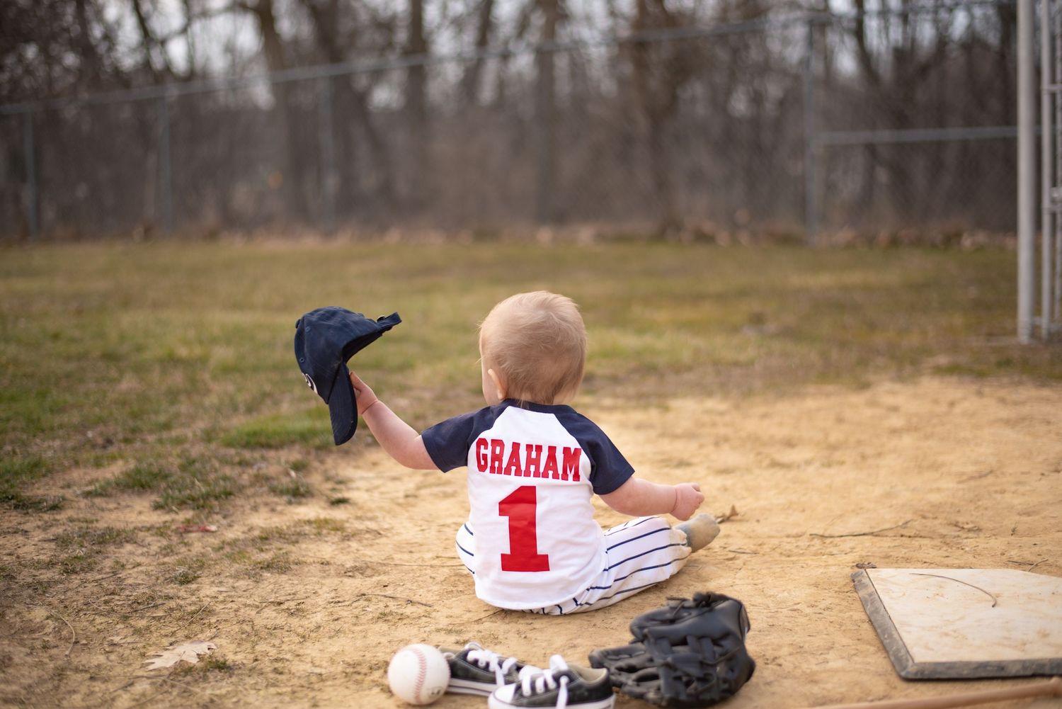 first birthday boy sitting near the mound holding a baseball hat