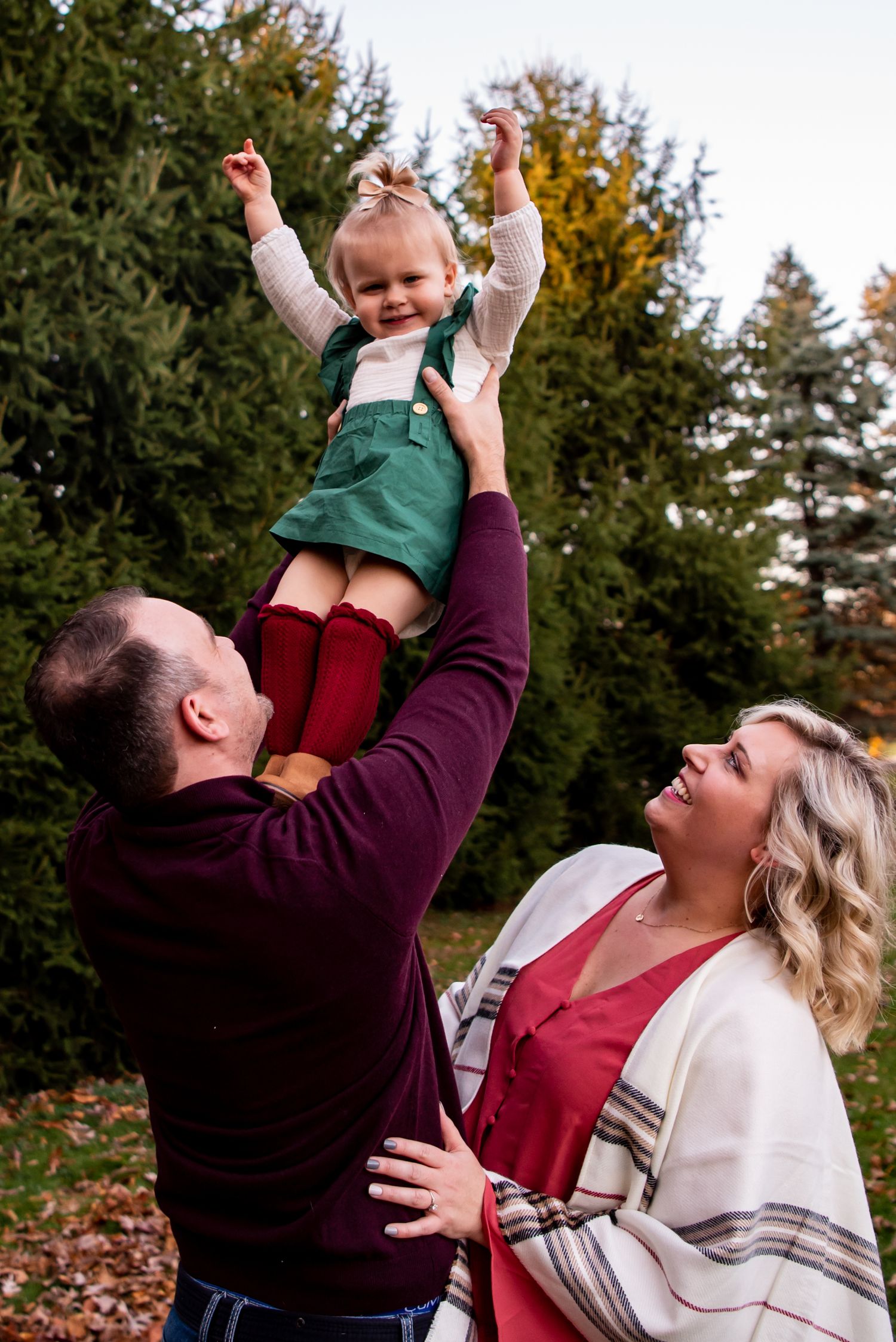 dad tossing toddler up as she laughs and mom is looking at dad