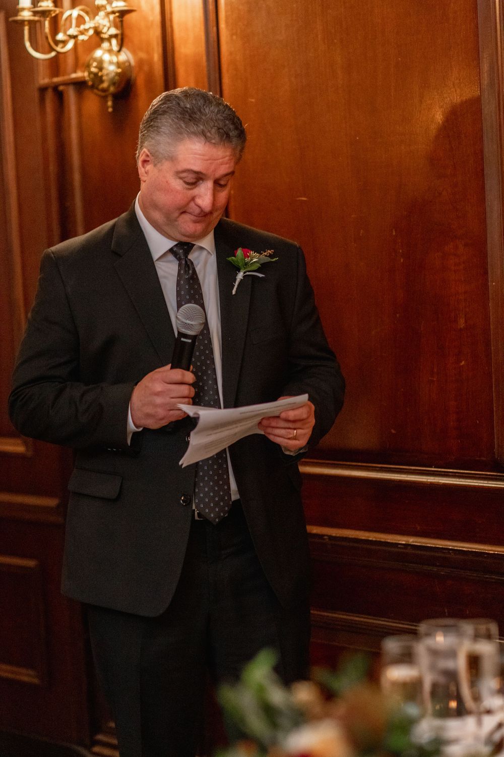 Speaker in dark suit reads from papers during formal reception speech.