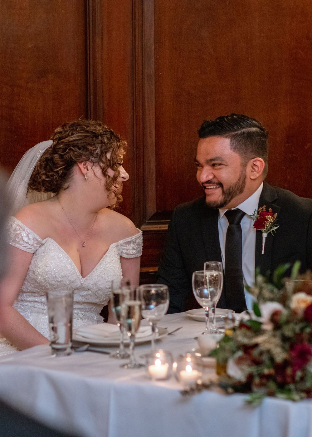 Couple shares joyful conversation at candlelit wedding reception table.